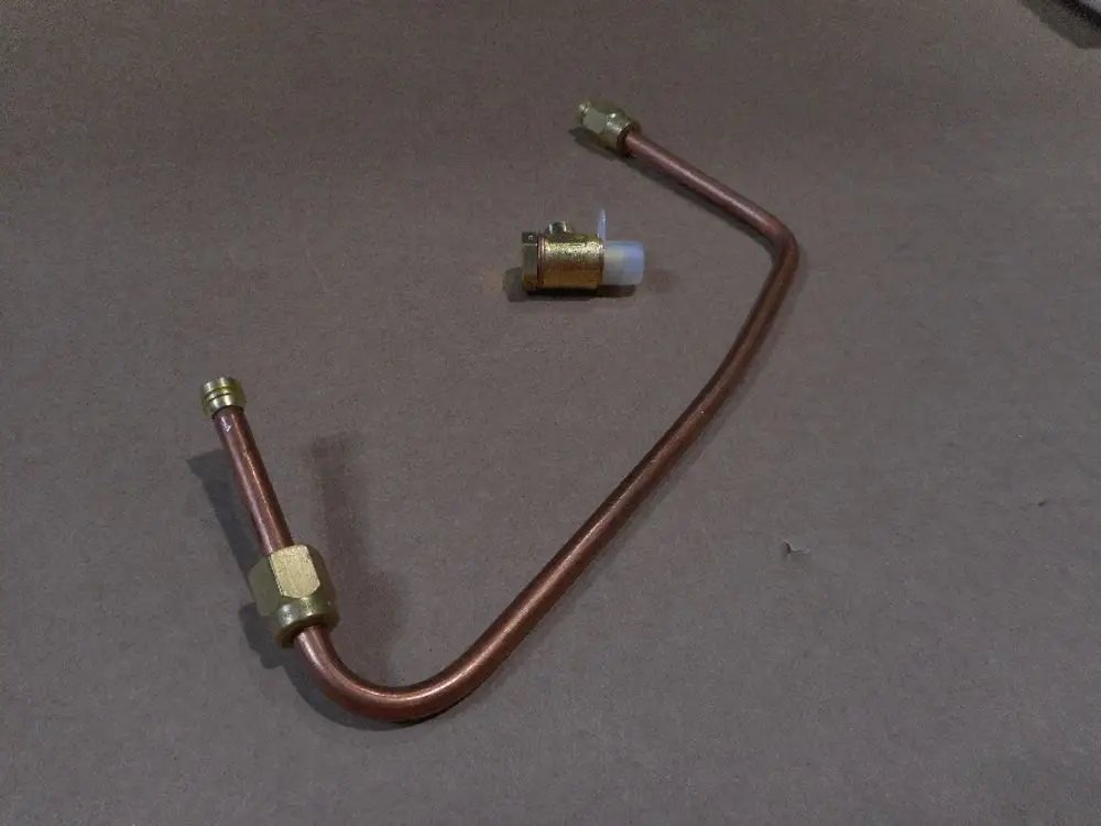 Ölzuführungsrohr aus Kupfer mit Messinganschlüssen, vermutlich von Remeha, auf braunem Hintergrund. Ein Bauteil zur Verbindung in Heizsystemen.
